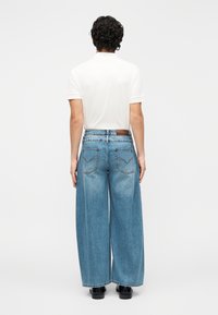 Vaqueros de corte ancho en azul claro con cintura alta. Presentan dos bolsillos traseros y un acabado texturizado. Combinados con una camisa blanca.