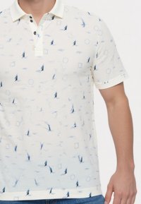 Kortærmet polo skjorte i off-white med et sejlbådsmønster. Har en kontrastfarvet krave, tre knaplukninger og en blød tekstur.
