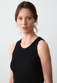 Top senza maniche nero a costine con scollatura rotonda. Il tessuto ha una consistenza liscia e la vestibilità è aderente, evidenziando la silhouette.