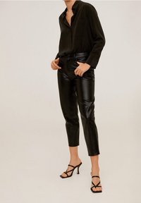 Chemise en satin noir, pantalon fuselé en simili cuir et talons aiguilles noirs. Texture lisse, design minimaliste, sans motifs visibles.