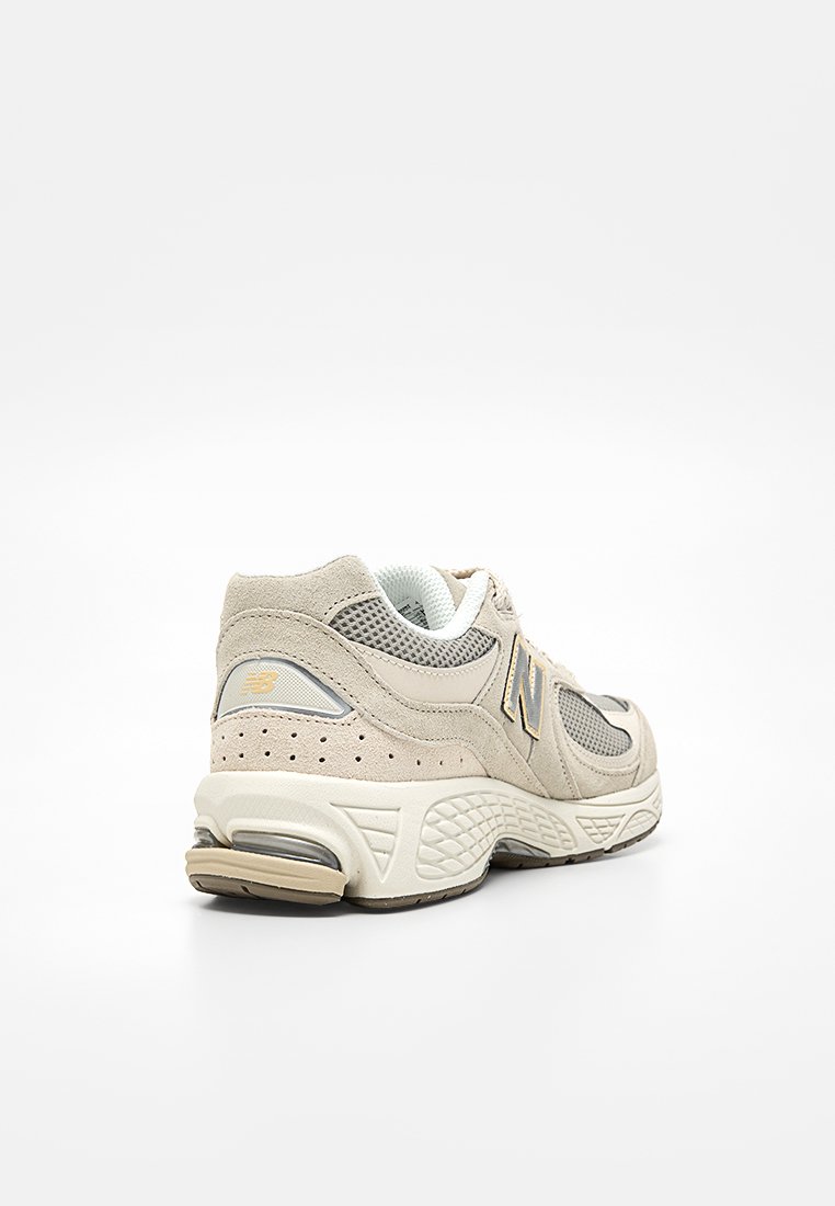 Sneaker New Balance in rete beige e grigia, angolata per mostrare i dettagli laterali e posteriori, suola imbottita e logo sul tallone e sul lato.