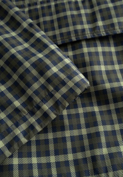 Primo piano di tessuto piegato con motivo a quadri blu scuro e verde chiaro caratterizzato da linee orizzontali e verticali che si intersecano.