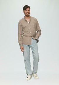 Lichtbruin knoopshirt, lichtblauwe ripped jeans en beige sneakers. De stof lijkt zacht met een relaxed fit. Eenvoudig ontwerp.