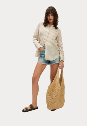Camicia a maniche lunghe beige a righe, pantaloni corti in denim blu chiaro, sandali neri con borchie e una borsa a tracolla intrecciata tan testurizzata.