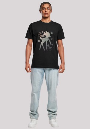 Svart bomull T-skjorte med et grafisk trykk av en hjorted silhouette med teksten "Such a doll" i sølv og hvitt på forsiden. Lette blå jeans er på.