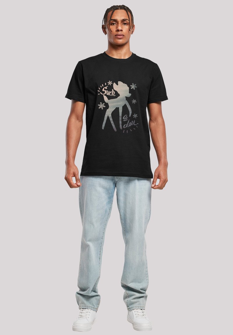 Svart bomull T-skjorte med et grafisk trykk av en hjorted silhouette med teksten "Such a doll" i sølv og hvitt på forsiden. Lette blå jeans er på.