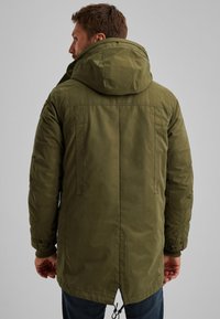 Maslinasto zeleni parka kaput s kapuljačom, s drškom na rubu, bočnim džepovima i rebrastim manžetama. Glatka vanjština s suptilnim detaljima šavova.