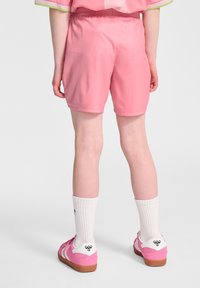 Rosa idrottsshorts med elastisk midja, slät textur och kontrasterande ljusgrön trim, tillsammans med vita strumpor och rosa skor.