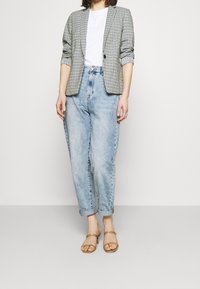 Blazer a quadri con maniche arrotolate su una maglietta bianca, abbinato a jeans chiari a vita alta e sandali color carne. Texture morbide e vestibilità casual.