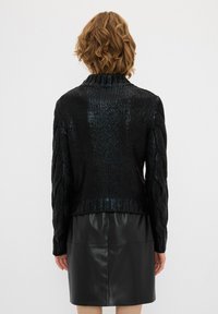 Schwarzer gestrickter Pullover mit strukturiertem Kabeldesign, mit hohem Kragen und gerippten Kanten, getragen über einem schwarzen Lederrock.