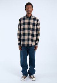 Camisa de franela a cuadros en negro y beige con cuello, cierre de botones y mangas largas, combinada con vaqueros de mezclilla azules holgados.