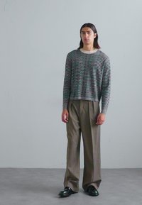 Pullover scurt, ușor, cu un model de text multicolor; purtat cu pantaloni khaki cu talie înaltă și picioare largi, și mocasini negri.