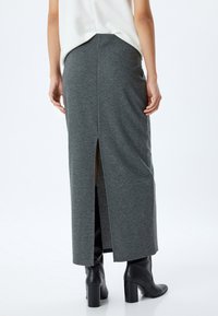 Gonna grigia, lunga fino al ginocchio, con una fessura sul retro centrale. Realizzata in tessuto morbido ed elasticizzato. Indossata con stivali neri con tacco. Design semplice e aderente.