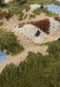 Tissu en laine présentant un motif camouflage dans des teintes de vert, beige, marron et bleu clair, avec une finition texturée et des fibres douces.