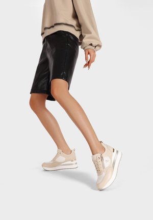 Sneakers atletici beige caratterizzati da una combinazione di tessuto morbido e pelle, con una suola bianca spessa e sottili dettagli dorati, che mostrano un design moderno.