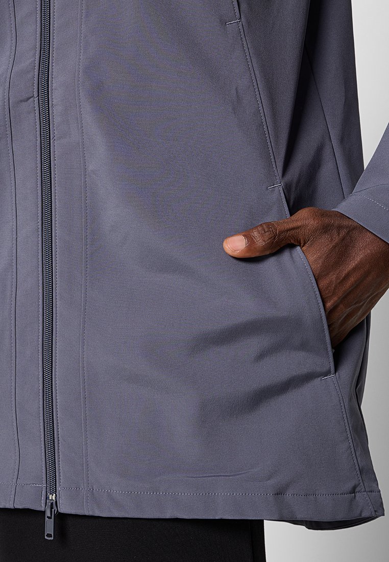 Veste gris clair avec une fermeture éclair et des poches latérales. Tissu lisse et léger avec une finition mate et sans motifs ni embellissements visibles.