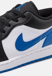 Černé kožené tenisky s bílými a modrými syntetickými akcenty, texturovaná podrážka, šněrovací design, s výrazným modrým logem Nike.