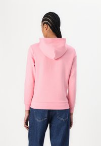 Lys rosa hettegenser med stor hette, lange ermer og ribbestrikkede mansjetter og hem. Har en glatt tekstur og et enkelt design.