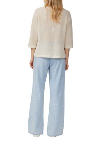 Top lavorato a maglia beige chiaro con un ampio motivo a trama aperta, maniche a tre quarti, abbinato a jeans in denim azzurro chiaro a gamba larga.