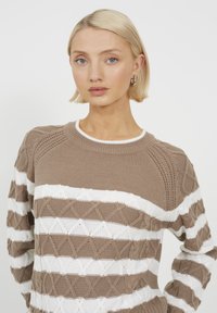 Brązowy i biały sweter z dzianiny w paski z teksturowanymi wzorami, z okrągłym dekoltem i ściągaczami.