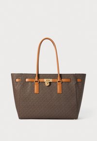 Bolsa de tote marrón con monograma y acentos de cuero caramelo, herrajes dorados, dos asas largas y un diseño estructurado.