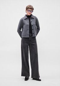 Casaco de mistura de lã cinza com gola e botões na frente, combinado com calças de ganga de perna larga pretas de cintura alta e botas ankle pretas.