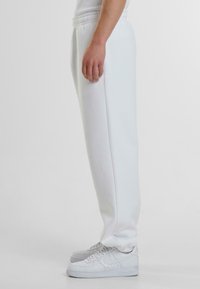 Witte joggingbroek met een taps toelopend ontwerp, elastische tailleband, gladde textuur en zijzakken, gecombineerd met witte sneakers.
