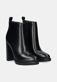 Botas de cuero negro hasta el tobillo con un acabado suave, tacones altos de bloque, cierre de cremallera en el lateral y lengüetas en la parte posterior para facilitar su uso.