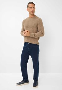 Pull en maille marron avec une texture côtelée, associé à un jean bleu foncé. Des baskets noires et blanches complètent la tenue.