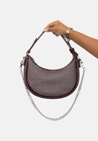 Bolso de piel burdeos con diseño perforado, forma curva y asa de cadena plateada, con cierre de cremallera y asa de piel.