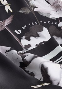 Fekete alapon fehér és szürke virágmintás selyem anyag, szitakötőkkel és a "b by Ted Baker" logóval modern betűtípussal.