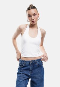 Witte haltertop van zachte stof, gecombineerd met losse blauwe denim jeans. De top heeft een brede halslijn en een kortere lengte.