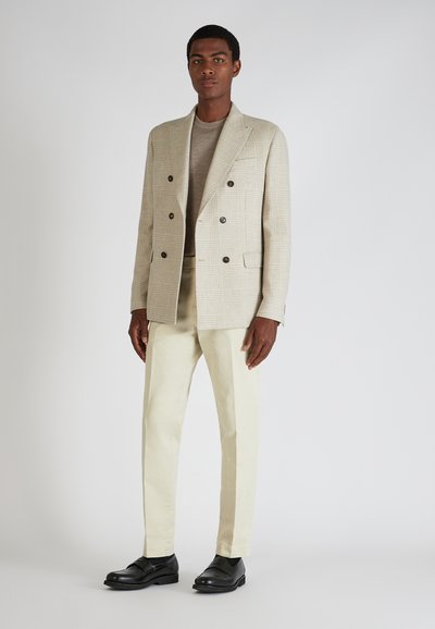Blazer de doble botonadura de cuadros en beige claro, suéter beige, pantalones crema y zapatos negros, con una textura suave y un corte ajustado.