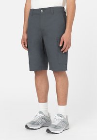 Shorts cargo gris foncé en tissu texturé, avec deux poches latérales, une fermeture à bouton et une coupe décontractée. Associés à des chaussures de sport grises.
