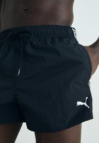 Črne kopalne hlače iz lahkega blaga. Imajo elastičen pas z vrvico in beli Puma logotip na robu. Minimalističen dizajn.