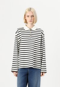 Striped long-sleeve polo shirt in black and white with a white collar and three decorative buttons. Relaxed fit, soft fabric.