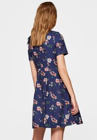 Lyhythihainen, tummansininen kukkamekko, joka on valmistettu kevyestä kankaasta. Mekossa on levenevä hame ja kukkakuosi punaisilla, valkoisilla ja vihreillä väreillä.