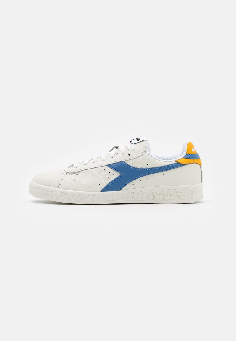 Vit lädersneaker med blå sidostrip och gul hälaccent, platt sula och vita snören, visad i profil på vit bakgrund.