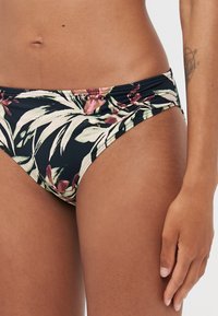 Blomstrete bikinitruse i svart med grønn, rosa og hvit botanisk trykk. Har en rynket midje og glatt tekstur.