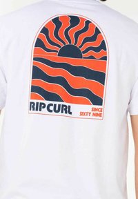 Weißes Baumwoll-T-Shirt mit einem Grafikdruck auf der Rückseite, der einen Sonnenuntergang, Wellen und den Text "RIP CURL SINCE SIXTY NINE" in fetter Schrift zeigt.
