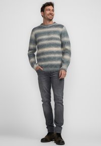 Suéter de punto a rayas en azul y beige, con cuello redondo, puños acanalados, combinado con jeans grises y botas de cordones marrones.