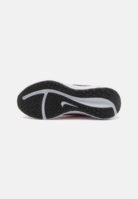 Semelle de chaussure de sport Nike avec une embase en caoutchouc noir offrant une bonne adhérence, dotée d'un motif texturé et d'accents blancs. Détails rouges visibles près du talon.