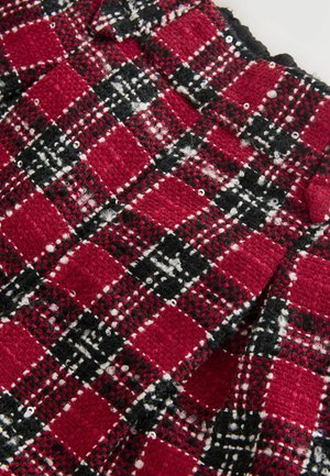 Țesătură texturată tweed roșie, neagră și albă cu un model în carouri și mici paiete, arătând o secțiune pliată și un buton din țesătură.