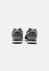 Pár čiernych a sivých tenisiek New Balance otočených smerom dozadu na bielom pozadí.