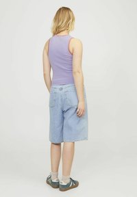 Top sin mangas morado con un ribete naranja en contraste, combinado con shorts de denim azul claro que llegan a la mitad del muslo, usados con zapatillas deportivas azules.