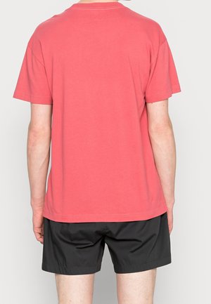 Korallenrotes Baumwoll-T-Shirt mit kurzen Ärmeln und rundem Ausschnitt, von hinten gezeigt. Kombiniert mit schwarzen Shorts. Einfarbig, lässige Passform.
