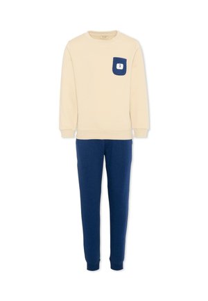 Top beige a maniche lunghe con tasca sul petto blu navy e pantaloni blu navy abbinati, stilizzato come un completo casual da indossare in casa.