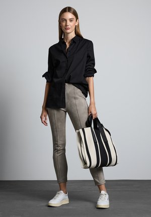 Zwarte button-up overhemd, grijze rekbare broek, witte sneakers en een grote crèmekleurige tas met zwarte strepen. Glad materiaal, slim fit.