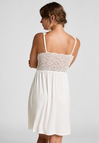 Camicetta da notte con schiena in pizzo, di colore crema, con spalline regolabili, presenta un corpino in pizzo aderente e un tessuto morbido e fluente sotto la vita.