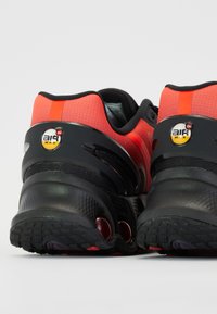 Baskets de sport rouges et noires avec une tige texturée, semelle en caoutchouc noire et détail de coussin d'air avec un logo circulaire.